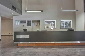 A reception desk with a dark counter, a computer, and a phone. There are framed pictures on the wall and a sign with business logos. - City Express by Marriott Ciudad de México Plaza Central (Mexico City)