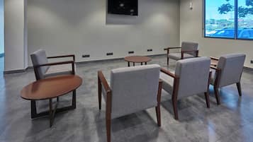 A conference room with a large TV on the wall, grey chairs, a round table, and a view of a parking lot through a large window.