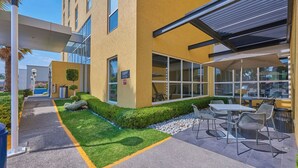 Un edificio moderno con fachada amarilla, zona de estar al aire libre y un sendero que conduce a la entrada.