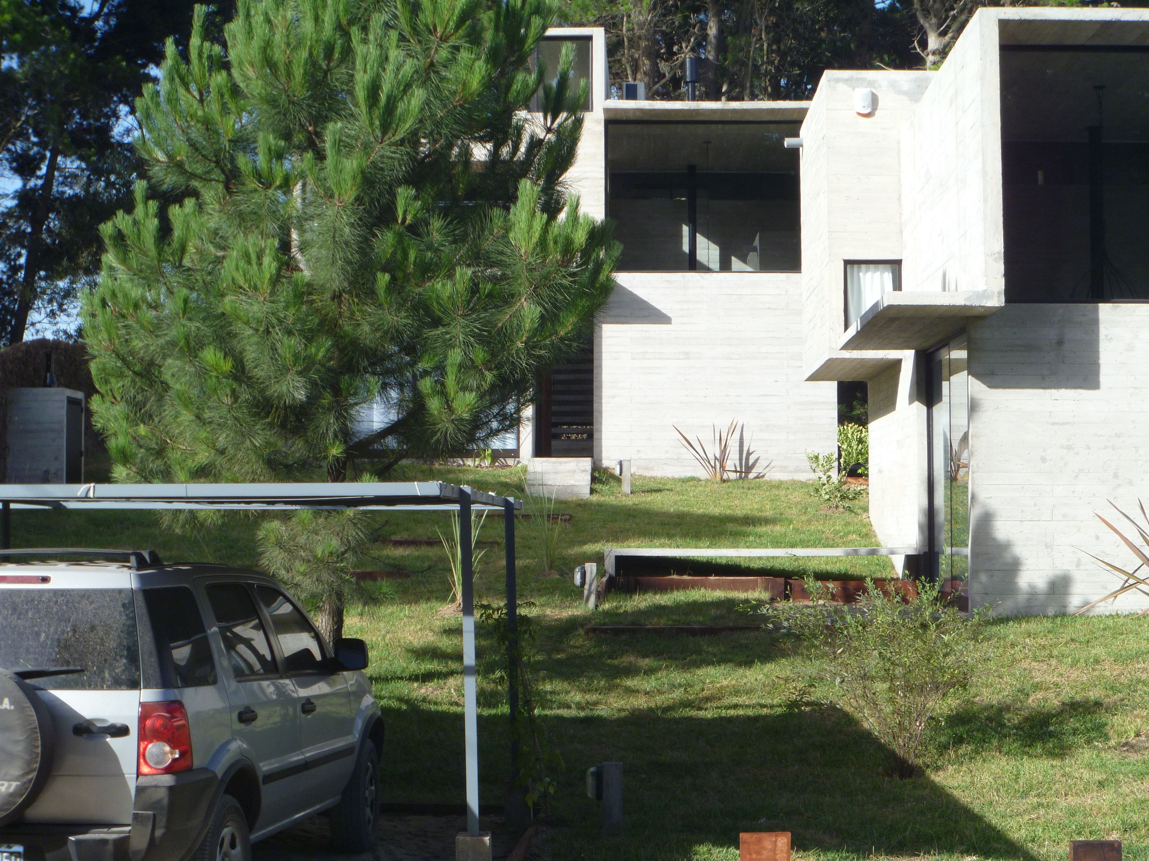 A modern building with a concrete exterior, a parked SUV, and a large pine tree in the foreground.