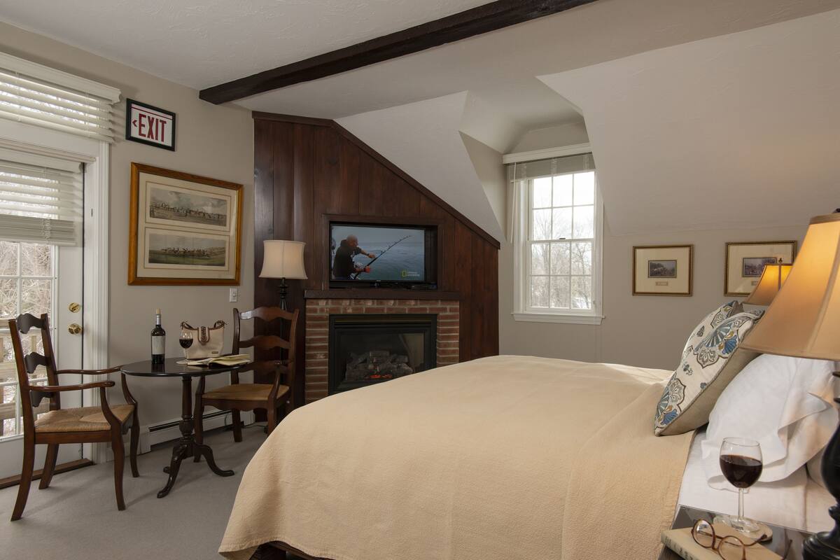 A bedroom with a fireplace, a television, a bed, and a dining area with chairs and a table.