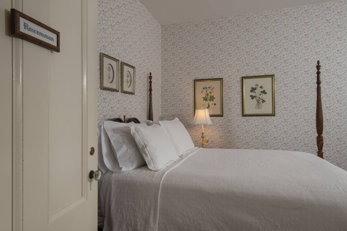 A bedroom with a bed, a bedside table with a lamp, and floral wallpaper.