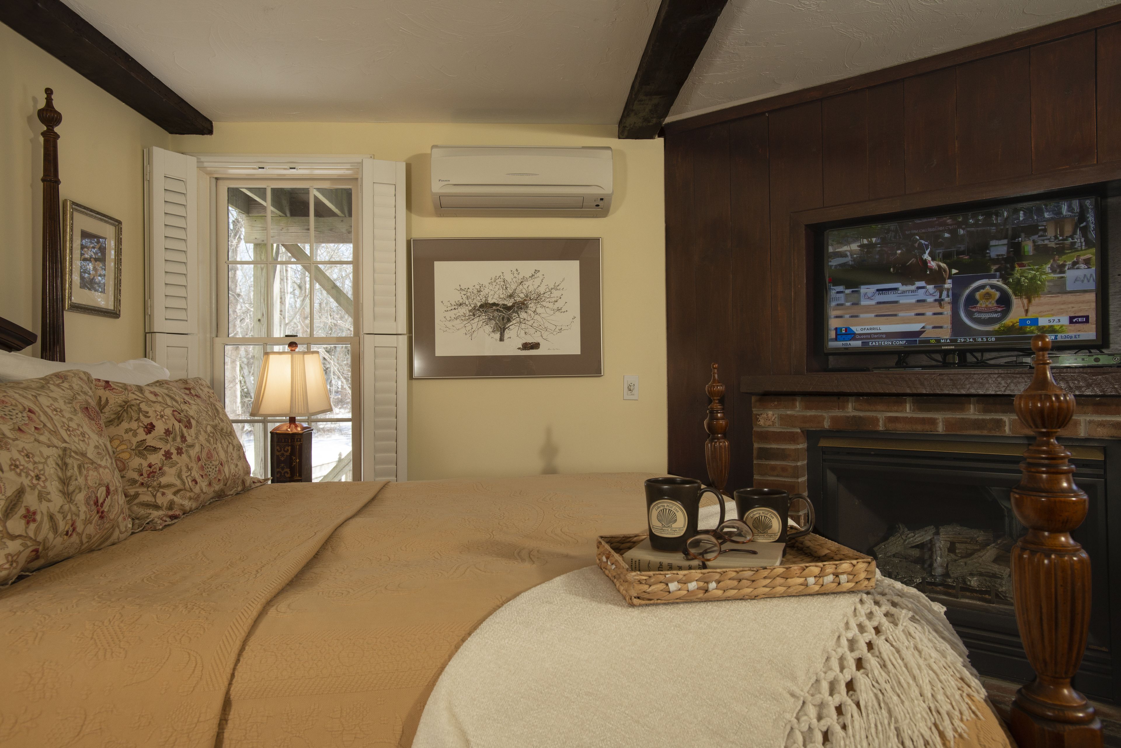 A bedroom with a bed, a fireplace, a television, and a window with shutters.