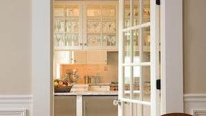 A kitchen with white cabinetry, a wooden floor, and a dining area with a table and chairs. - Liberty Hill Inn (Yarmouth Port)