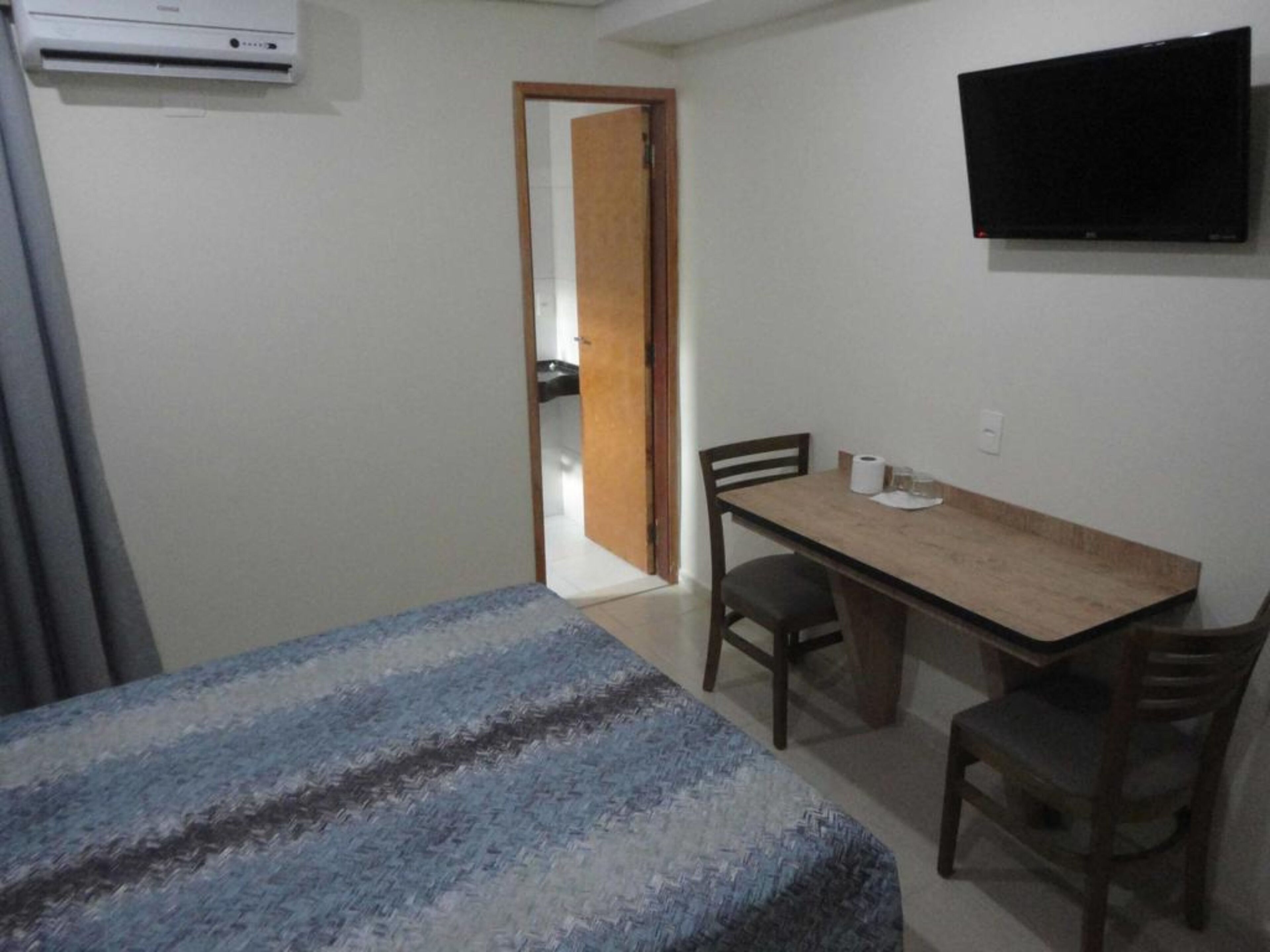 A small, sparsely furnished room with a bed, a desk, and a chair.