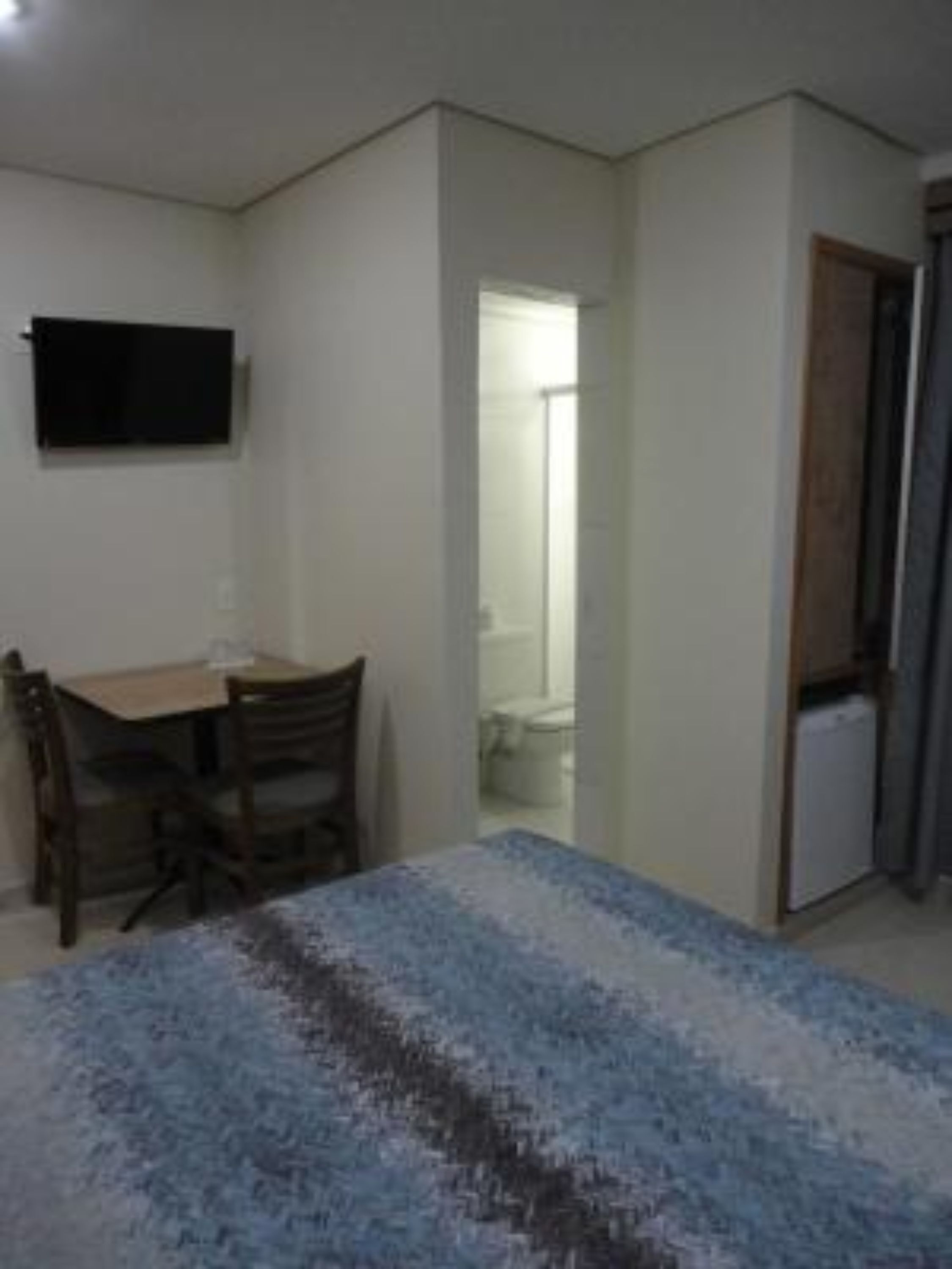 A small, sparsely furnished room with a bed, a desk, and a chair.