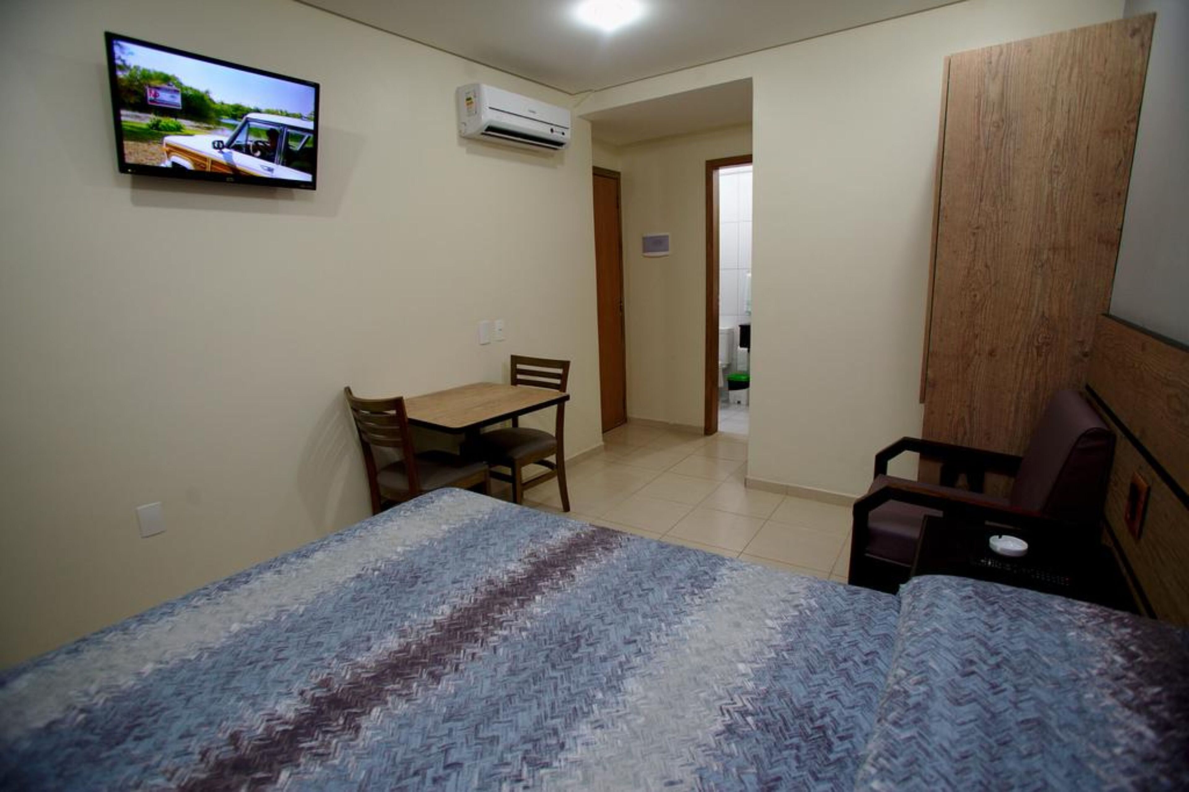 Una habitación pequeña con una cama, un escritorio, una silla y un televisor en la pared.
