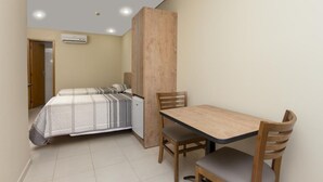 Una habitación compacta con cama, una pequeña mesa con sillas y un equipo de aire acondicionado en la pared.