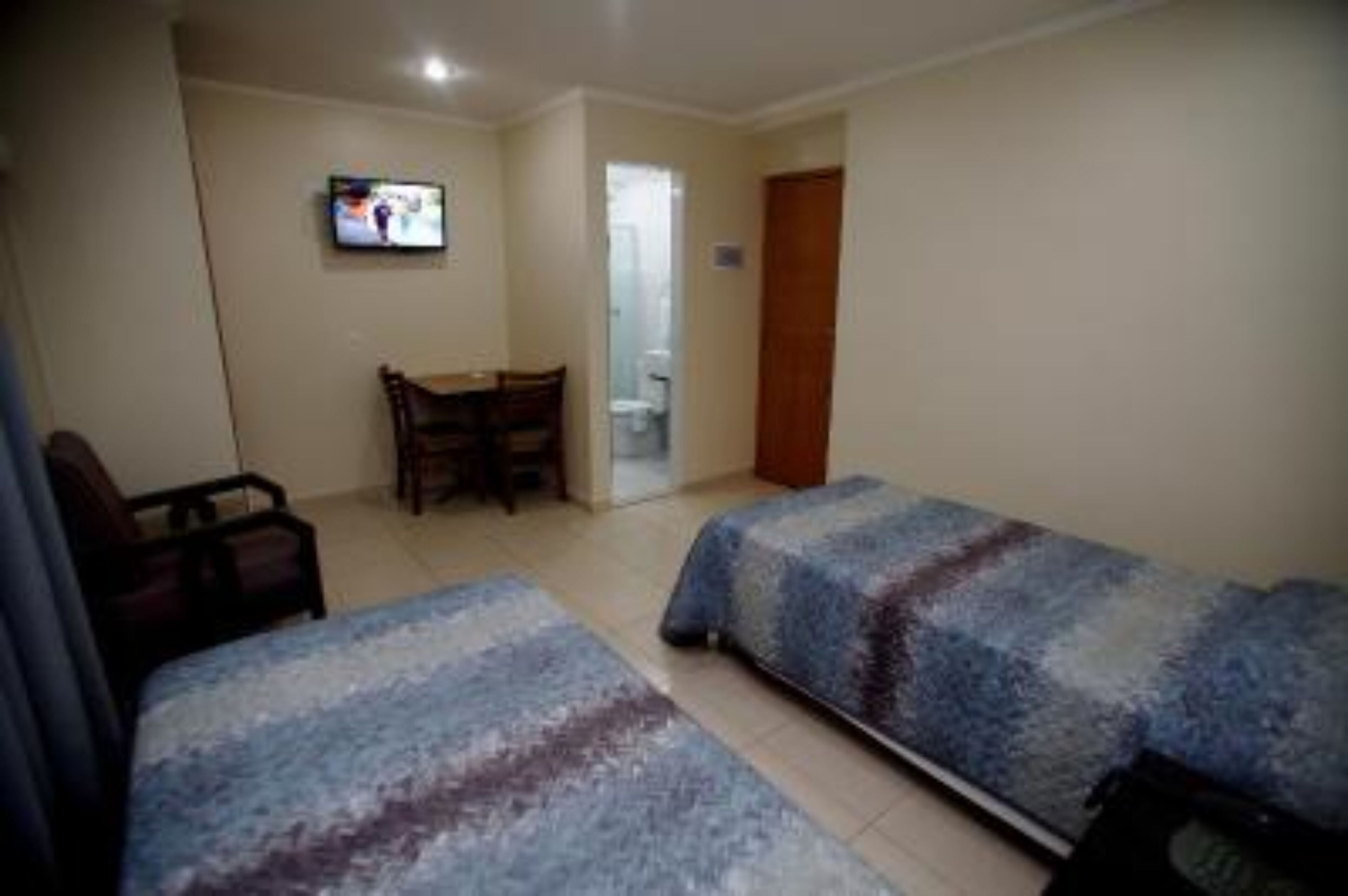 Ein Hotelzimmer mit zwei Betten, einem Fernseher, einem Schreibtisch und einem Sessel.