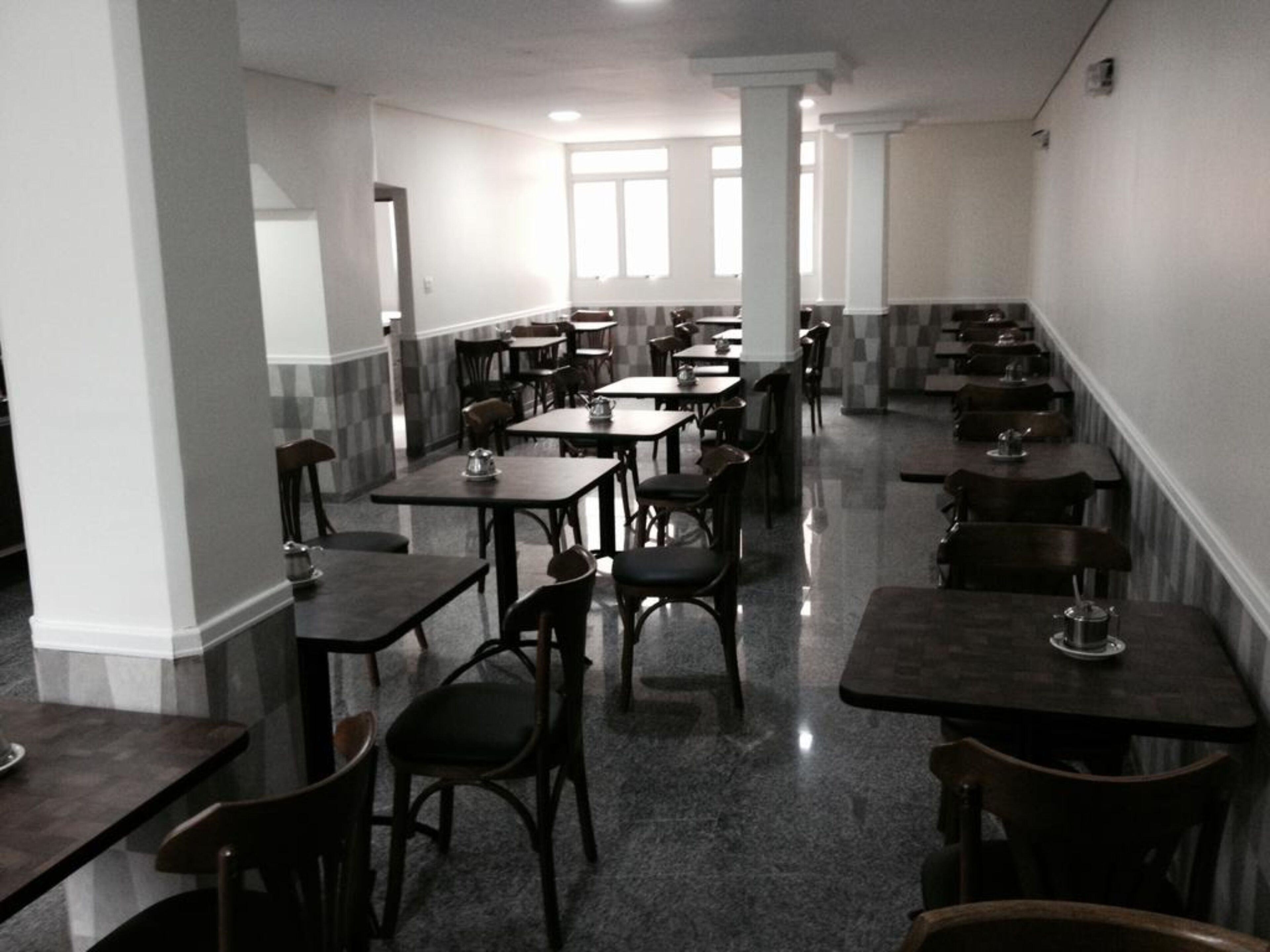 A spacious dining area with multiple tables and chairs, high ceilings, and large windows allowing natural light.