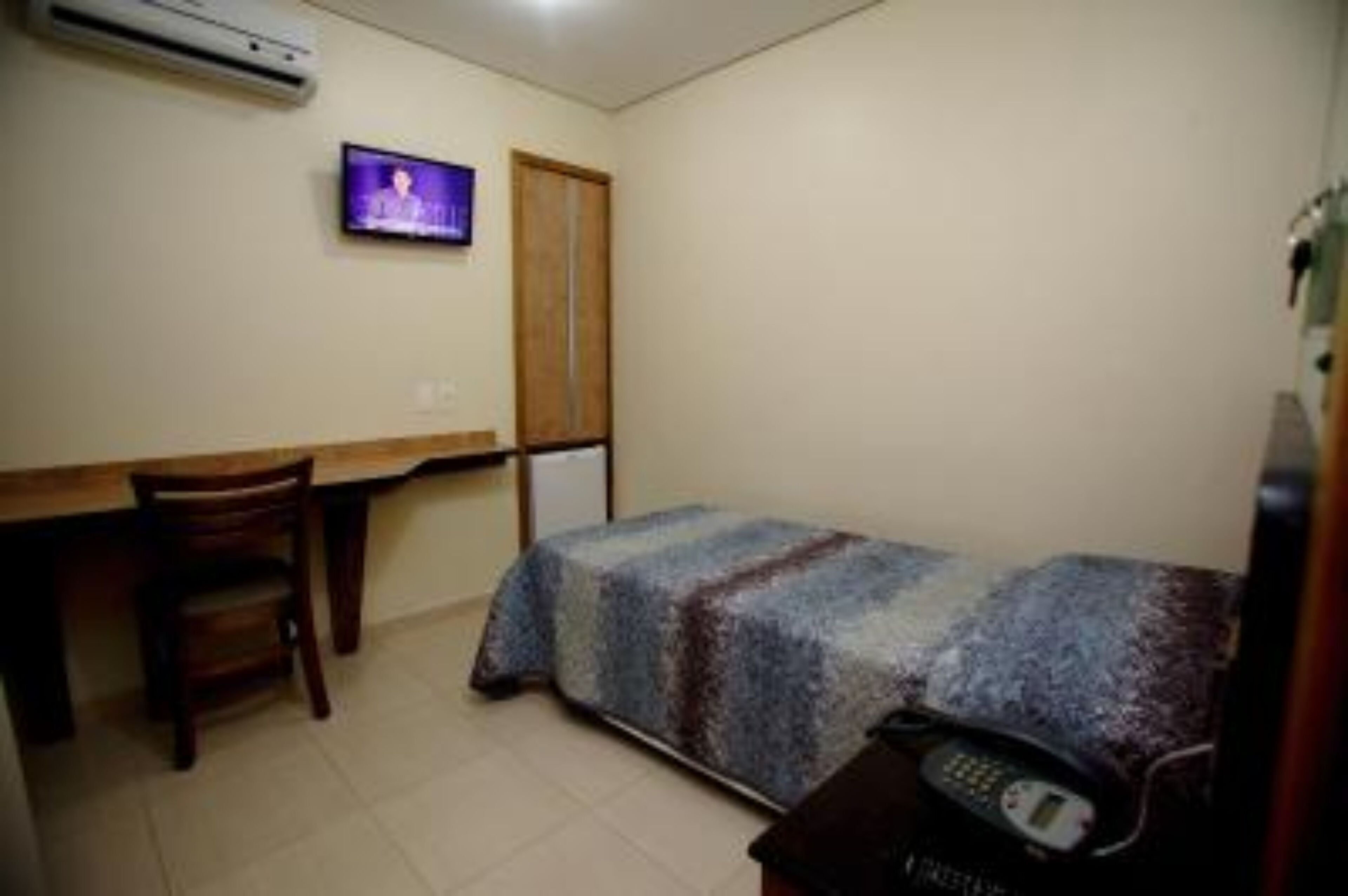 Una habitación pequeña y sencilla con cama, escritorio, silla, televisor y teléfono.