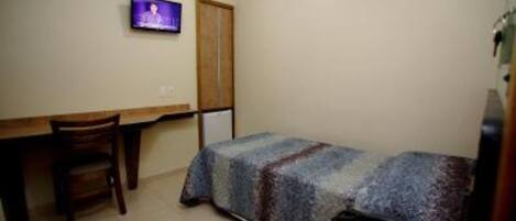 Una habitación pequeña y sencilla con cama, escritorio, silla, televisor y teléfono.