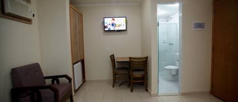 Una habitación con televisión, sofá, mesa y sillas, y un baño visible a través de una puerta abierta.
