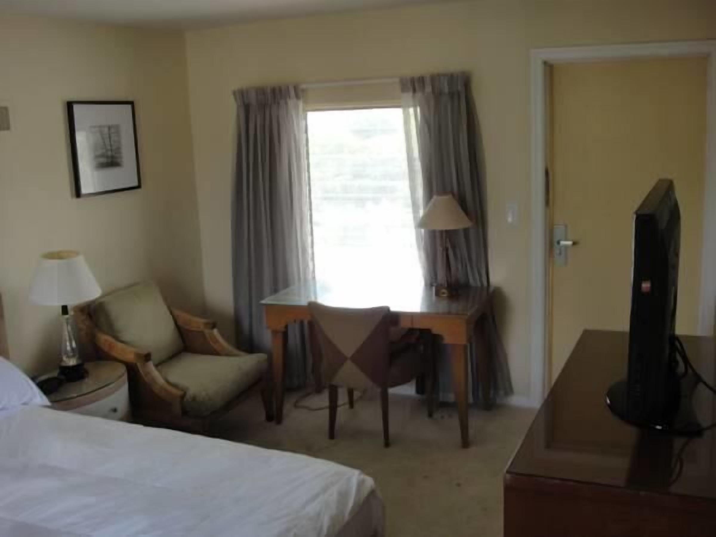 Een hotelkamer met een bed, een bureau met stoel, een televisie, een lamp en een raam met gordijnen.