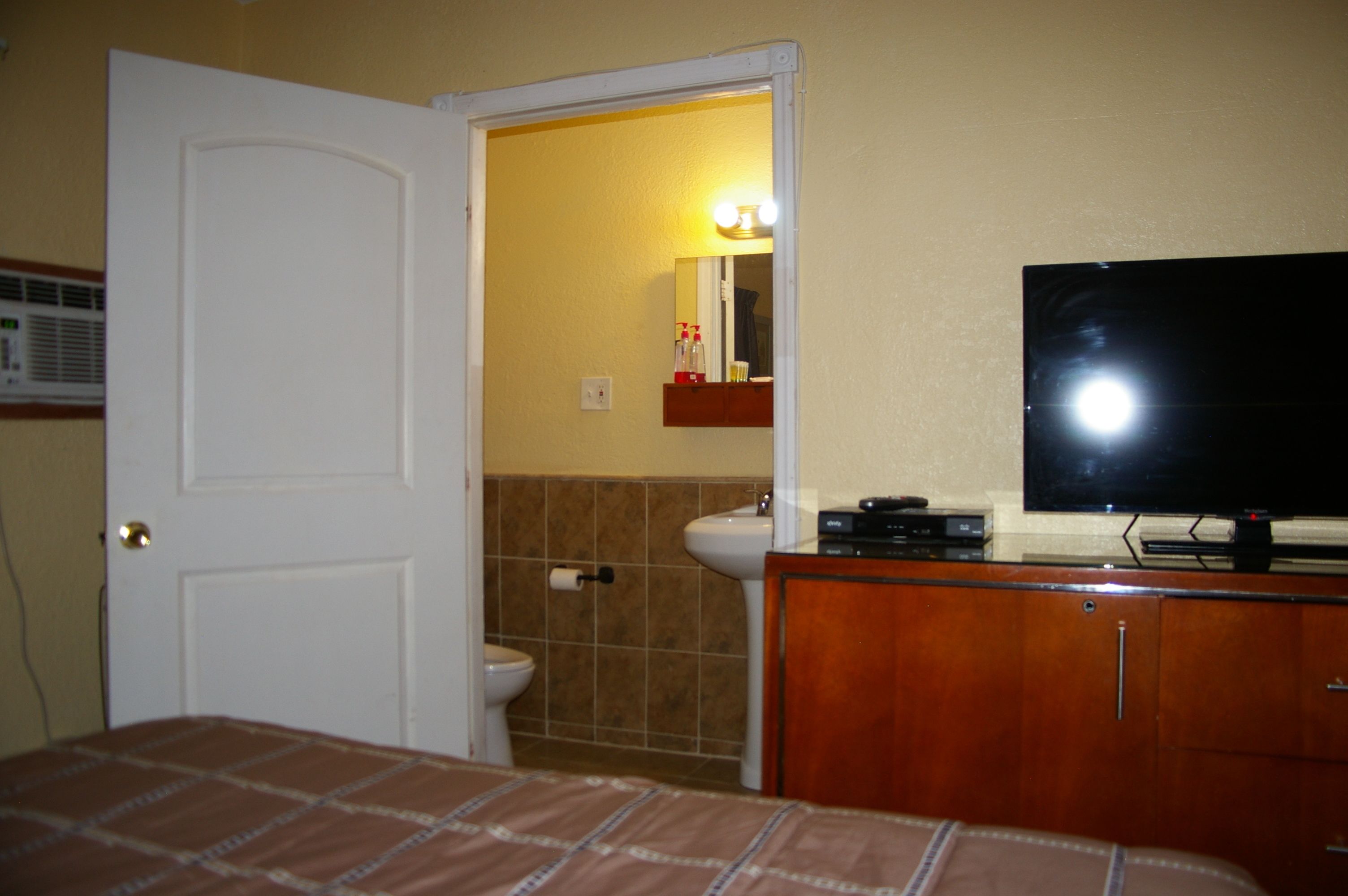 A hotel room with a bed, a television, a bathroom with a toilet and sink, and a mirror.
