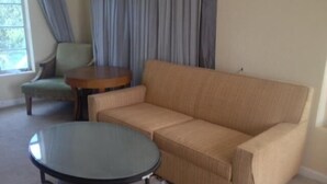 A living room with a beige sofa, a round table, and a small wooden side table. - Holiday House Motel (Lake Worth)
