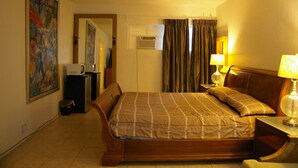 A hotel room with a bed, a nightstand, a lamp, a painting on the wall, and an air conditioning unit. - Holiday House Motel (Lake Worth)