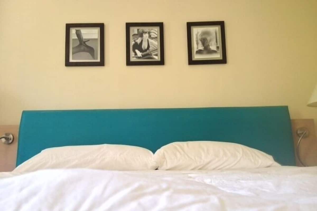 A bed with white bedding and a teal headboard in a room with three framed artworks on the wall.