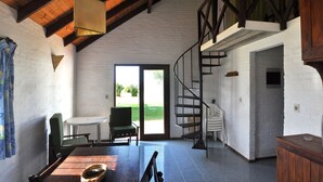 Une pièce spacieuse avec un plafond en bois, un escalier, un coin repas comprenant une table et des chaises, et une vue à travers une porte vitrée.