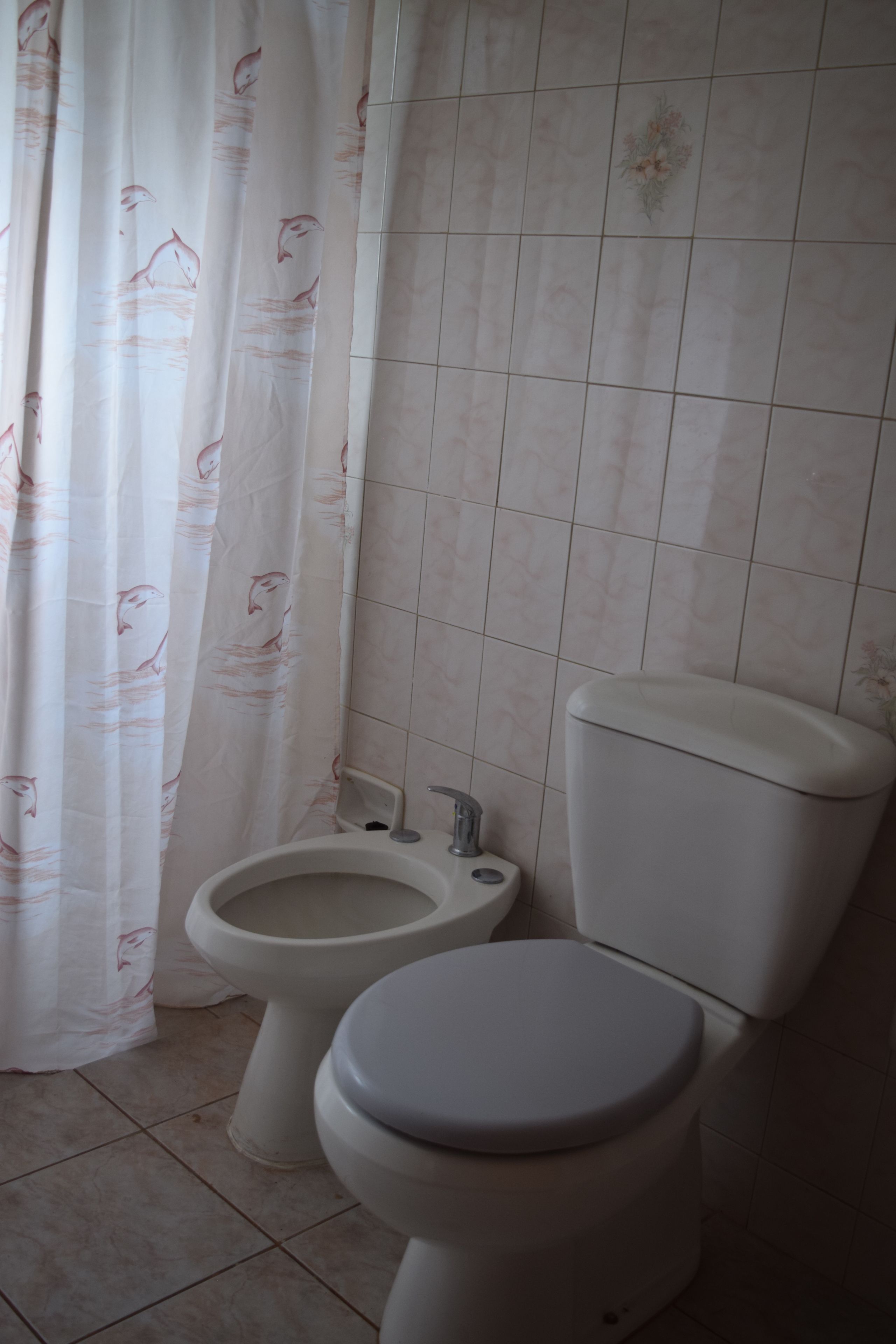 Une salle de bain équipée de toilettes, d’un bidet et d’un rideau de douche orné d’un motif de poissons.