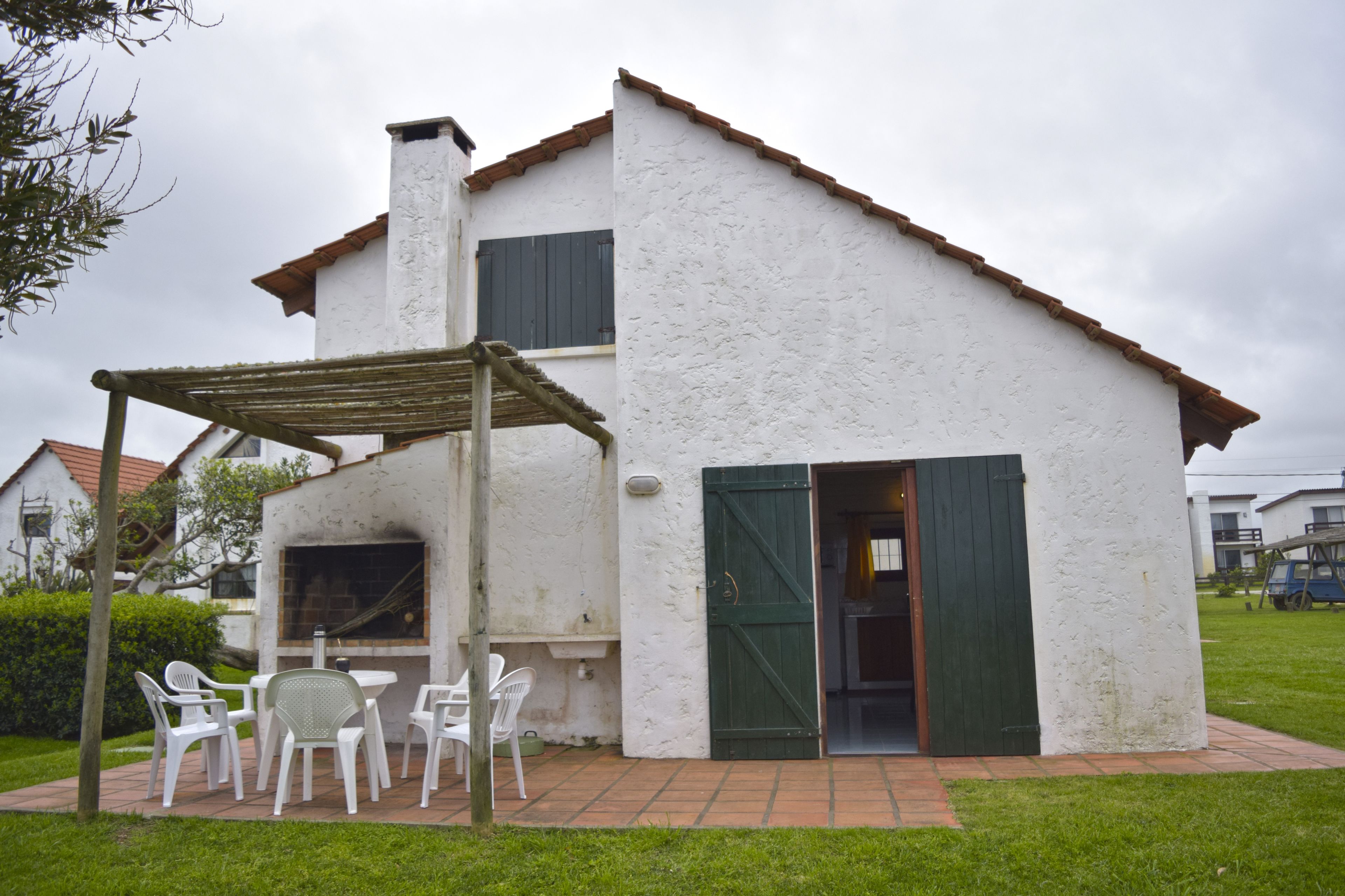 A two-story house with a white exterior and a green door. There is a patio with white chairs and a table.