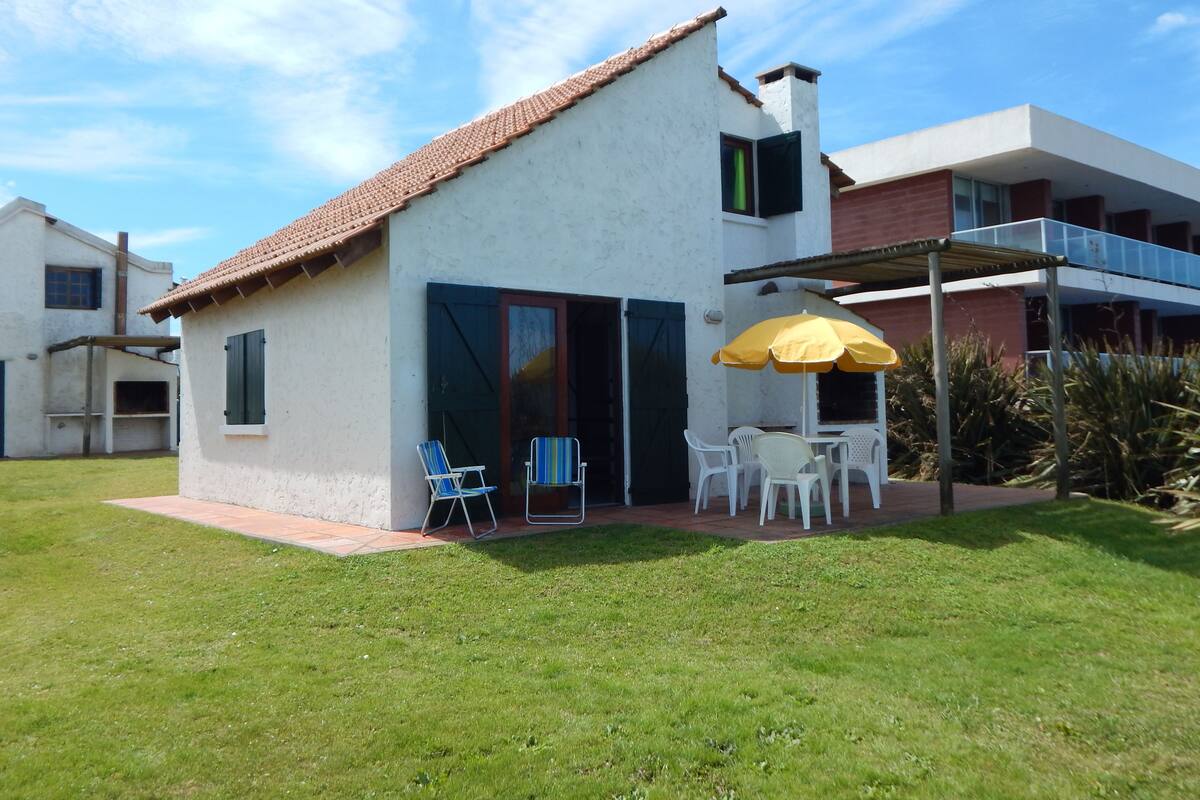 Une maison à deux étages, avec un toit recouvert de tuiles, une terrasse dotée de meubles d’extérieur et un parasol jaune.