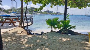 A beachside area with a wooden deck, a yellow chair, and a small palm tree.
