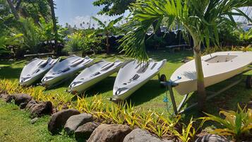 A row of jet skis parked on a grassy area with rocks and tropical plants.