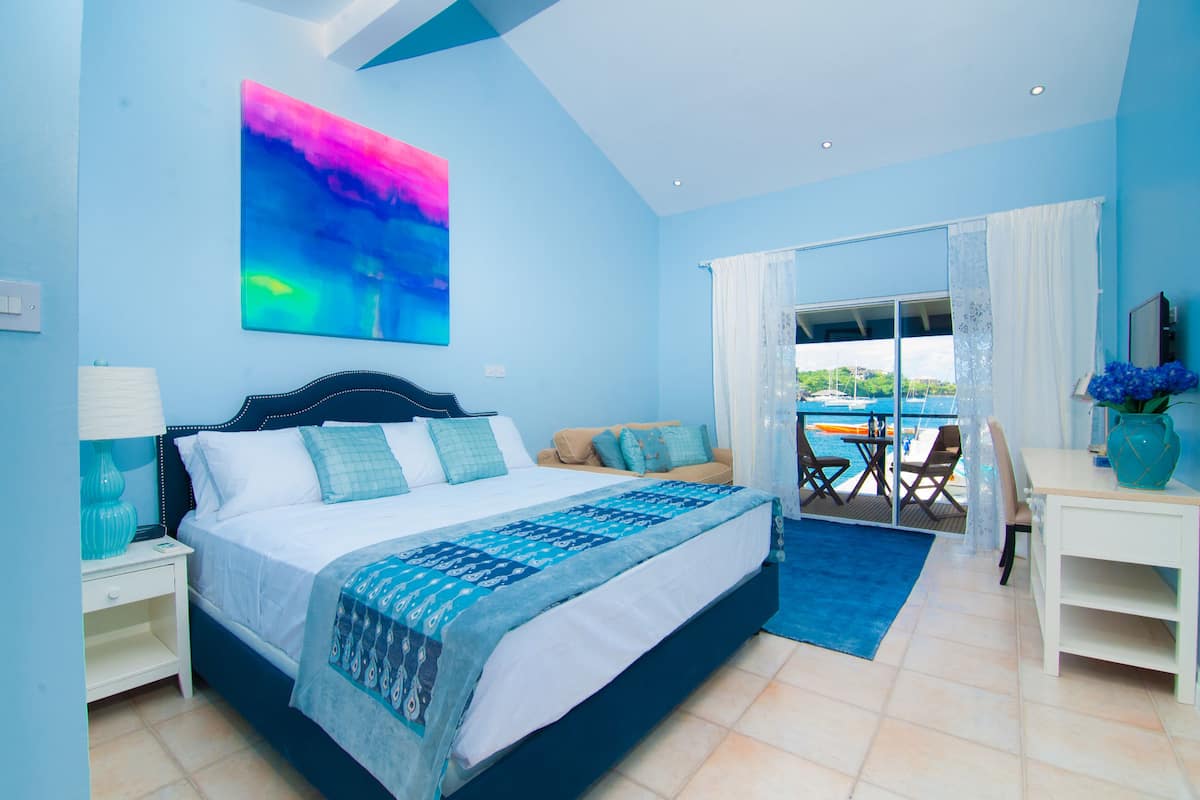Une chambre avec un lit, un bureau, une chaise, un balcon donnant sur la mer et un tableau accroché au mur.