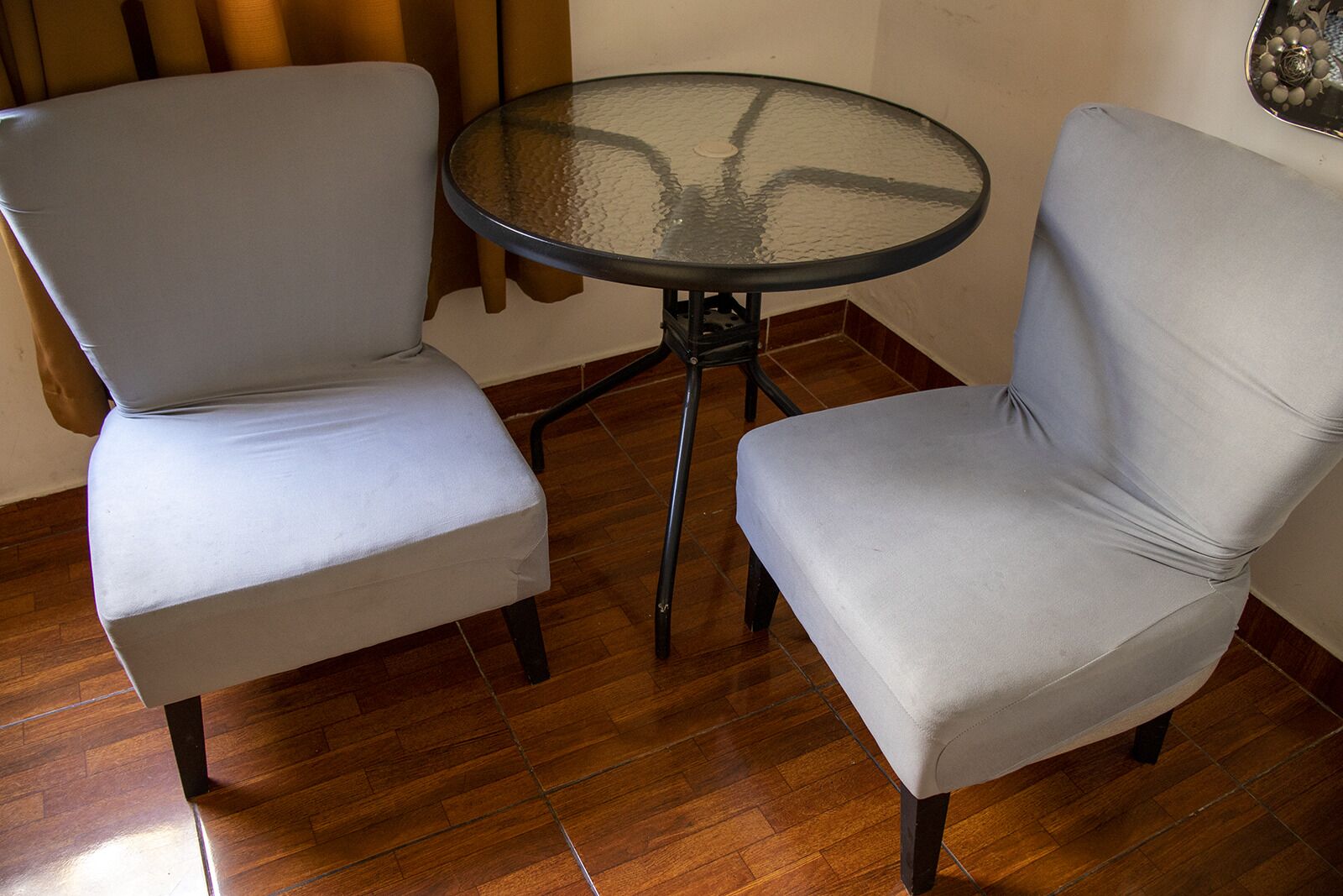 Dos sillones tapizados en gris y una pequeña mesa redonda de vidrio con estructura metálica.