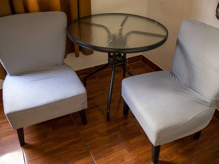 Duas cadeiras cinza estofadas e uma pequena mesa redonda de vidro com estrutura de metal.