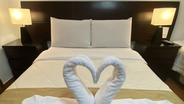 A hotel room with a neatly made bed, two bedside lamps, and a heart-shaped towel arrangement on the bed. - Plaza Mayor Lima (Lima)