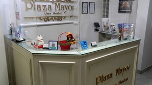A reception desk at Plaza Mayor Lima Hostel with a glass top, a decorative sign, and various items like a small statue, a basket, and informational brochures. - Plaza Mayor Lima (Lima)
