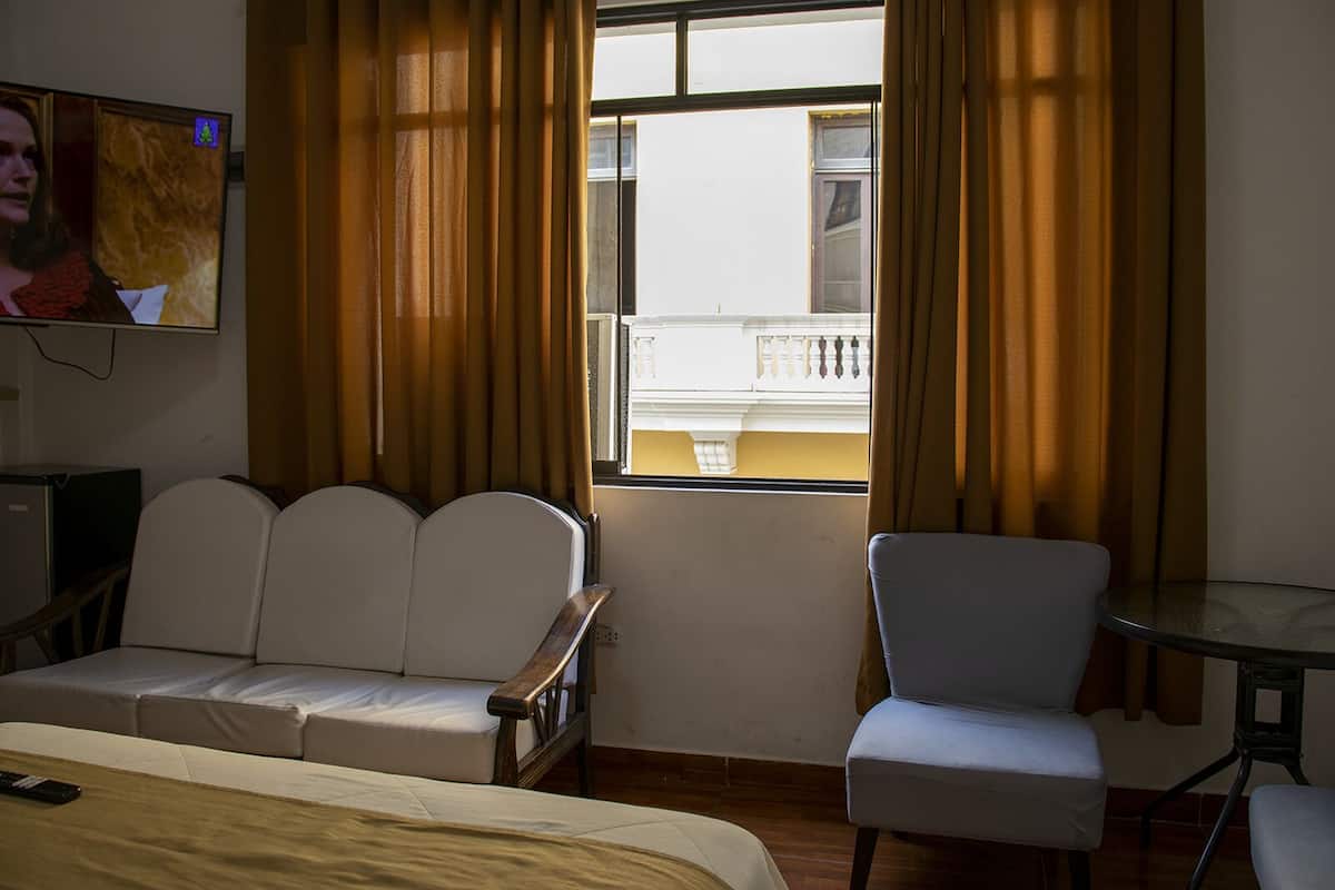A hotel room with a bed, a sofa, a chair, a small table, and a TV on the wall.