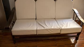A wooden sofa with a cushioned seat and backrest, positioned on a wooden floor.