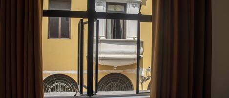 A window with a view of a yellow building with white trim and a balcony.