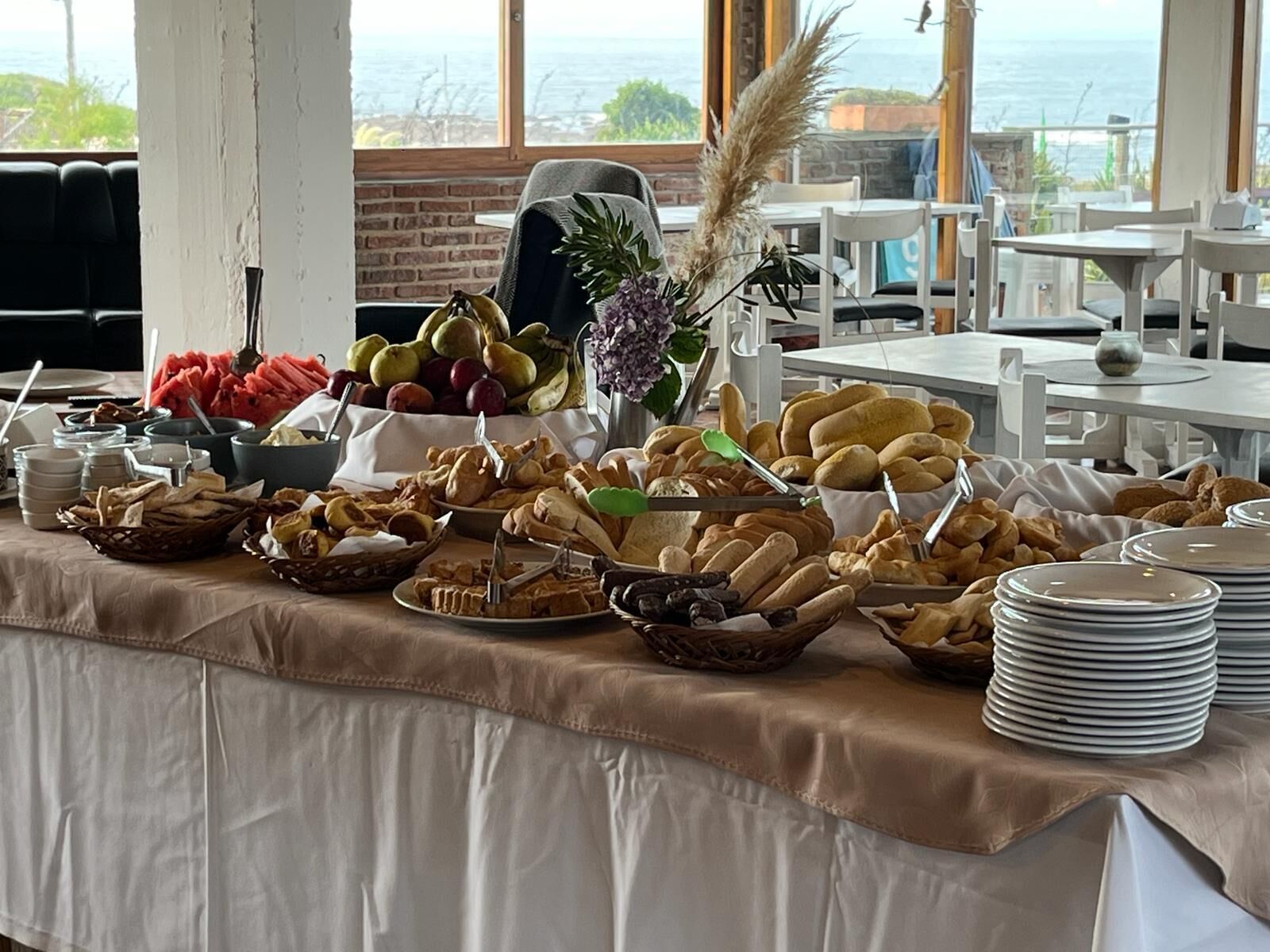 Una mesa de buffet con diversos alimentos y vista al océano a través de amplias ventanas.