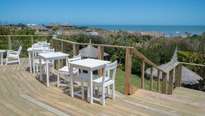 Una terraza de madera con mesas y sillas blancas con vista a una playa.