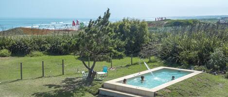 A swimming pool with a view of the ocean, surrounded by greenery and a fence.