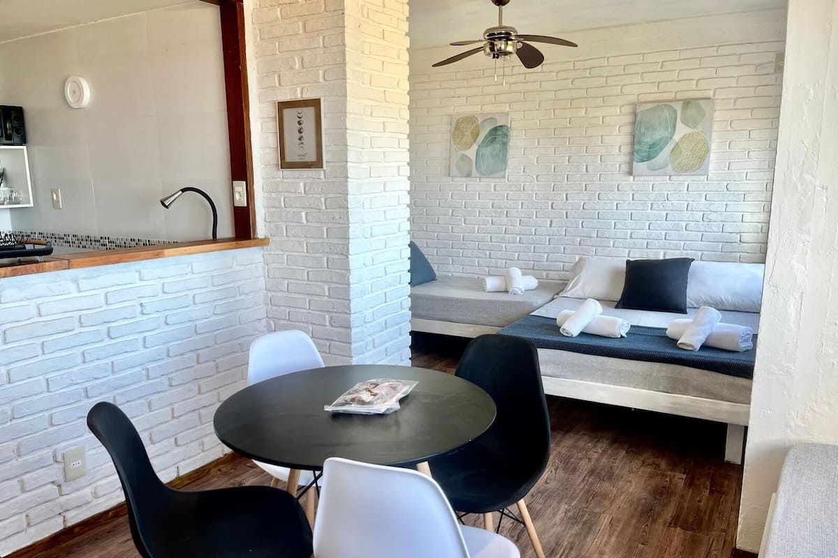 A compact room with a dining table, chairs, a sofa, and a ceiling fan.