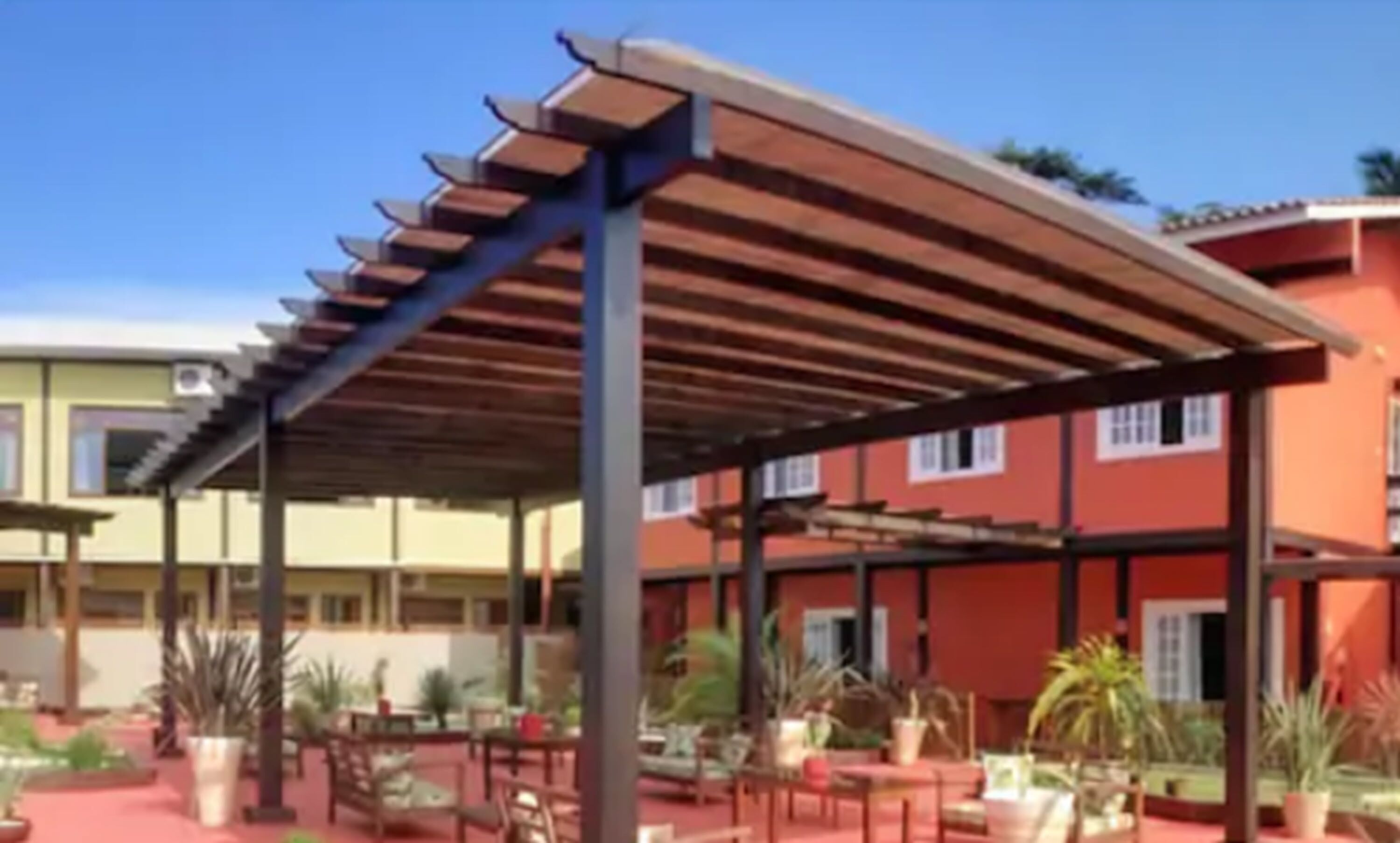 A covered outdoor area with tables and chairs, surrounded by potted plants.