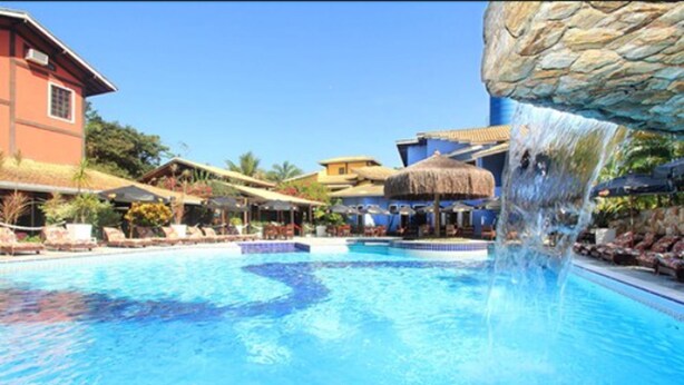 Piscina com cachoeira, rodeada por espreguiçadeiras e guarda-sóis.