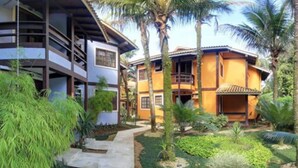 Um edifício de dois andares com varanda, cercado por vegetação exuberante e palmeiras.