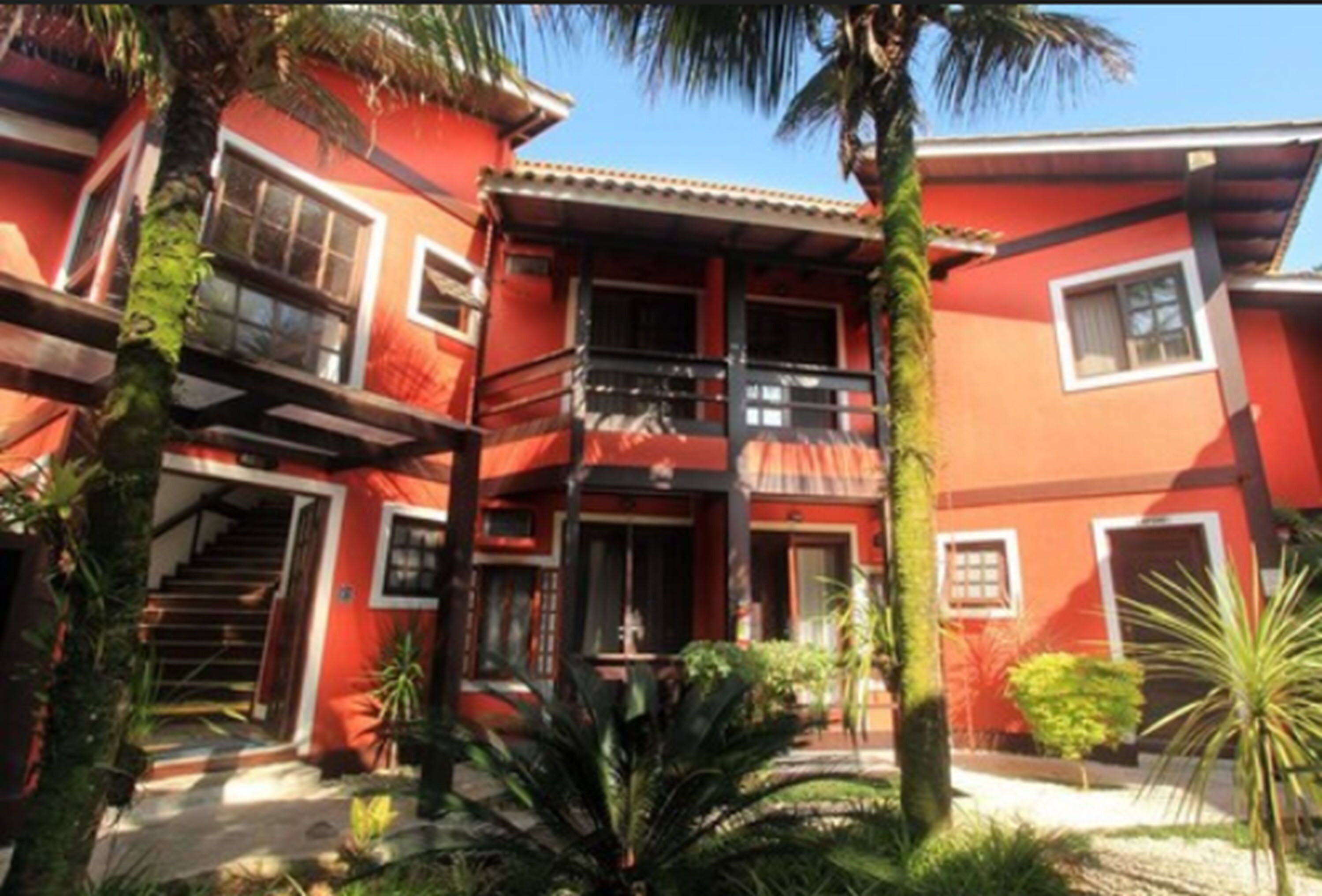 Edificio de dos pisos con balcón, rodeado de vegetación tropical.