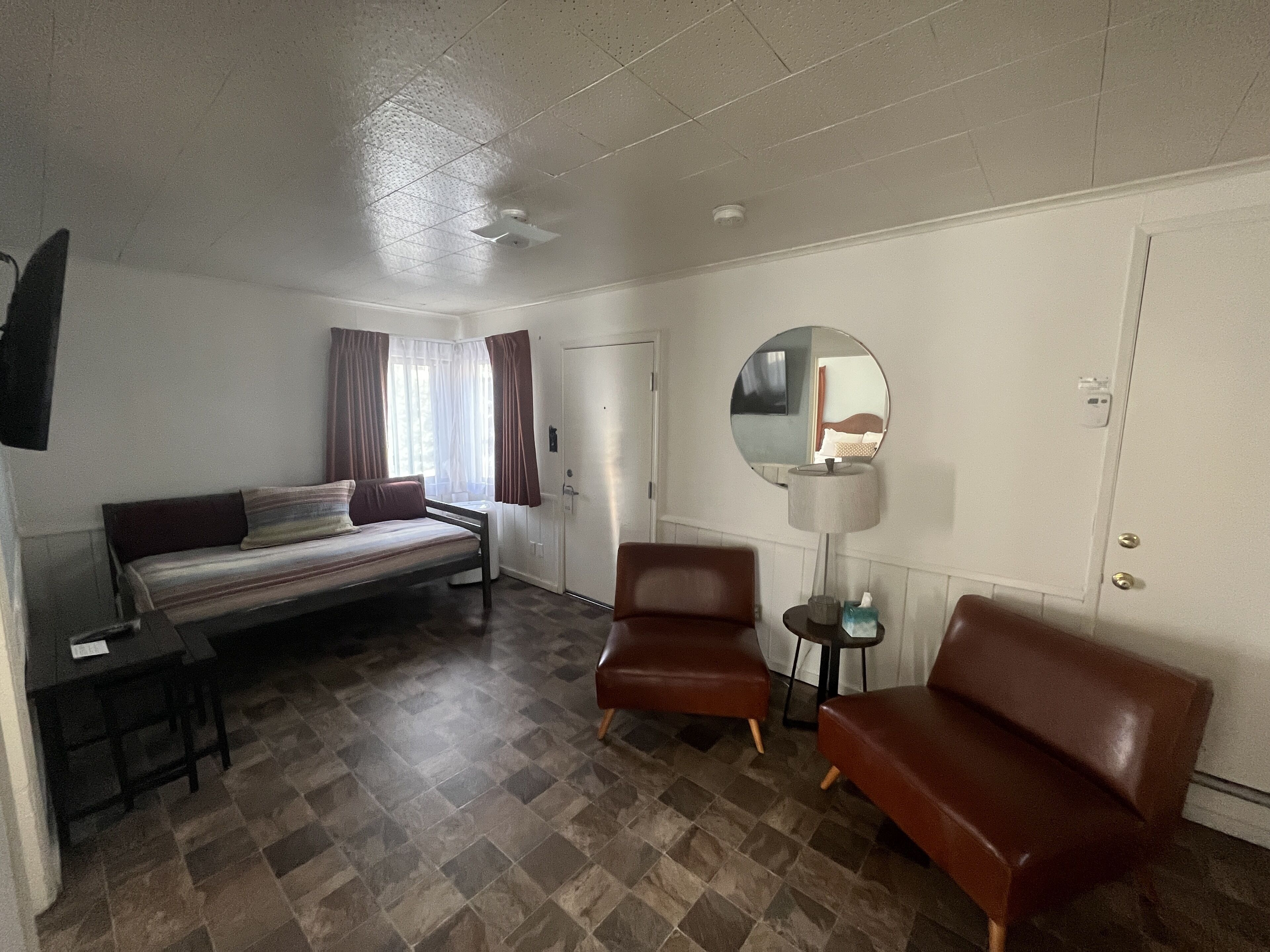 A room with a bed, two armchairs, a small table, a mirror, and a door.