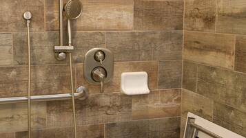 A shower area with a handheld showerhead, a wall-mounted control panel, and a handheld shower hose.