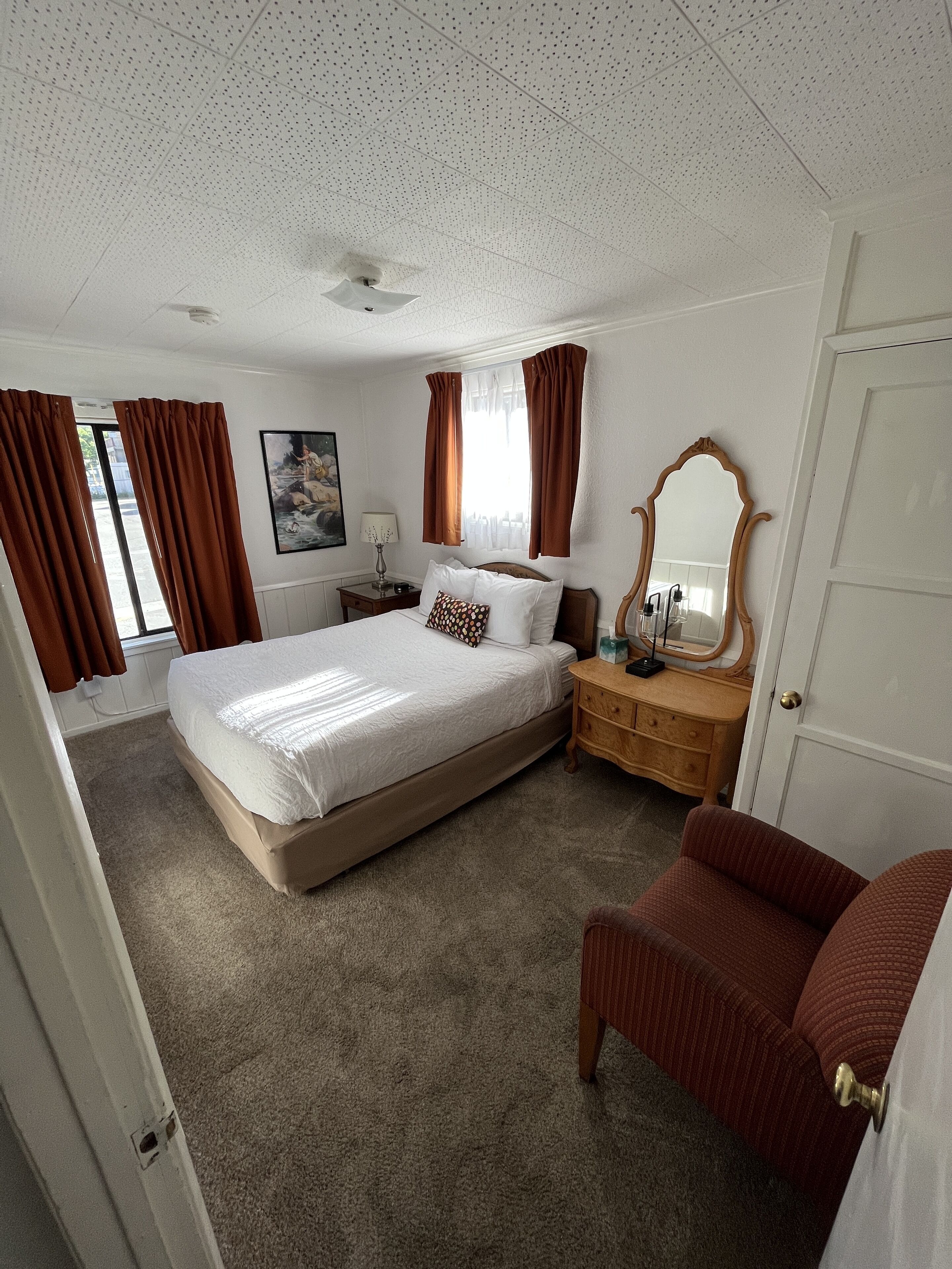 A bedroom with a large bed, a wooden nightstand, a dresser, a mirror, and brown curtains.