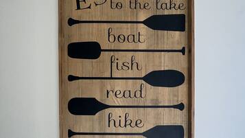 A wooden sign with the words "ESCAPE to the lake," "boat," "fish," "read," "hike," and "RELAX" arranged vertically.