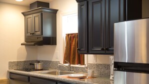 A kitchen with dark cabinets, a stainless steel refrigerator, a double sink, and a window with a colorful curtain. - June Lake Villager (June Lake)