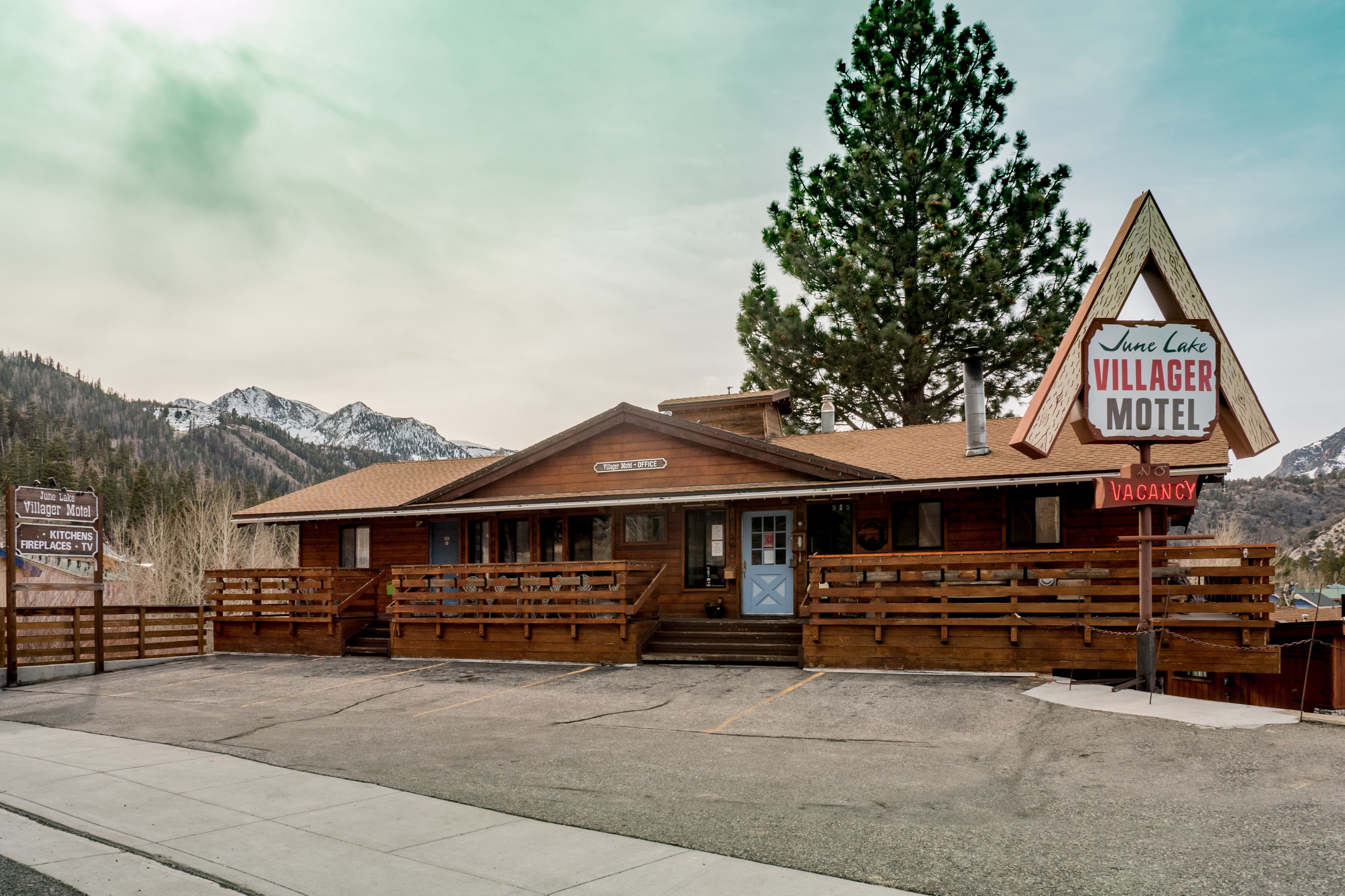 Un motel rustico con facciata in legno, un cartello che indica 'June Lake Villager Motel' e un cartello con scritto 'Nessuna camera disponibile'.